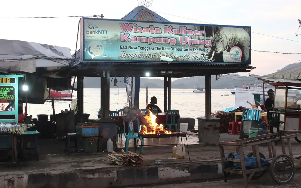 An open-air street food stall lit at night on the Labuan Bajo waterfront, with moored boats behind it.
