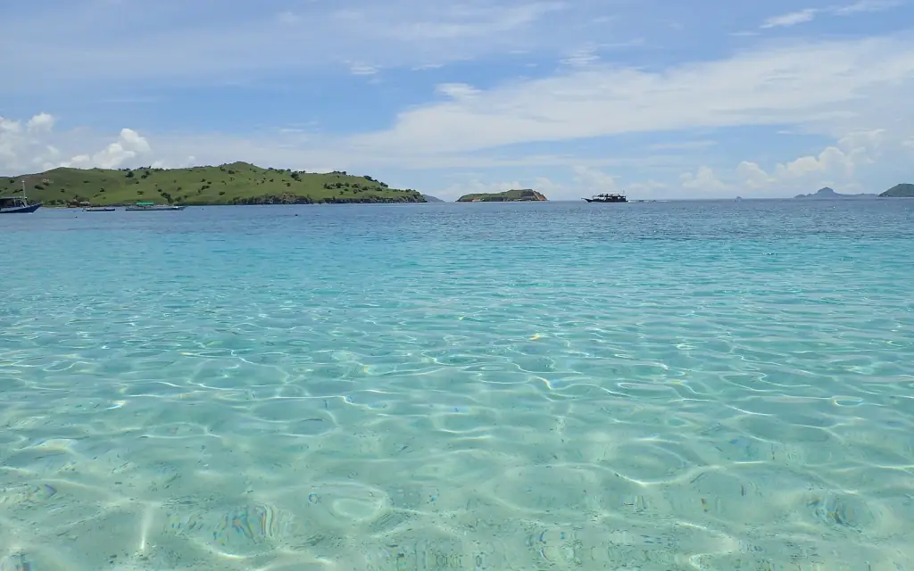 Clear, shallow turquoise water over sand off a low green island at Pink Beach, Komodo.