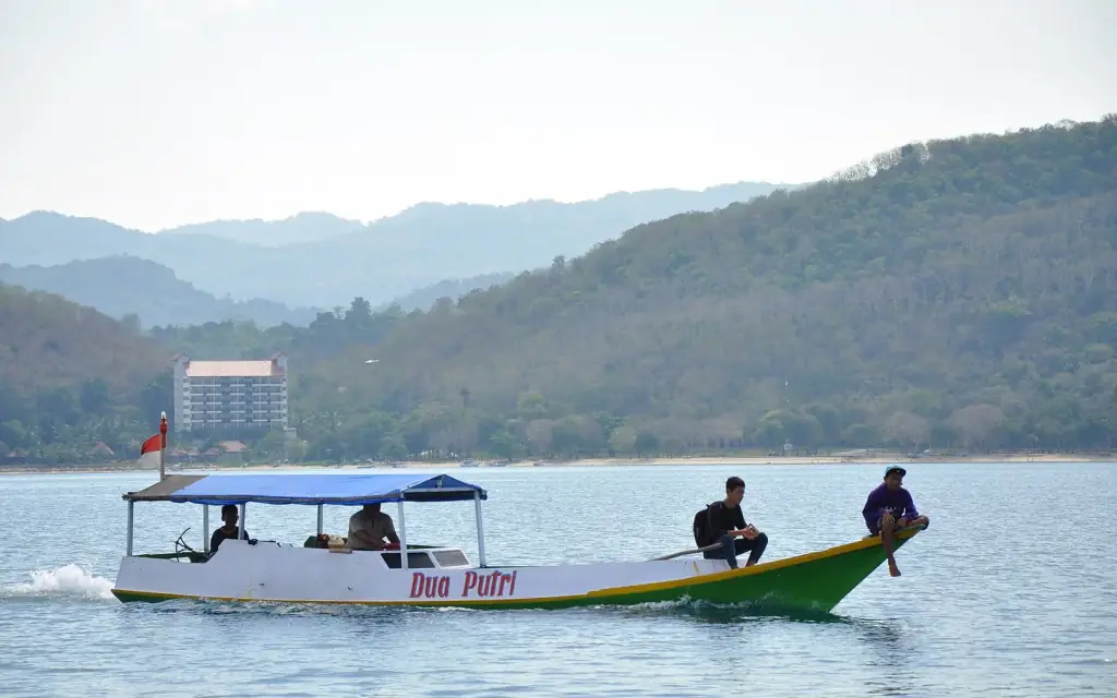 A small canopied wooden passenger boat carrying a handful of people across calm water, with Labuan Bajo behind.