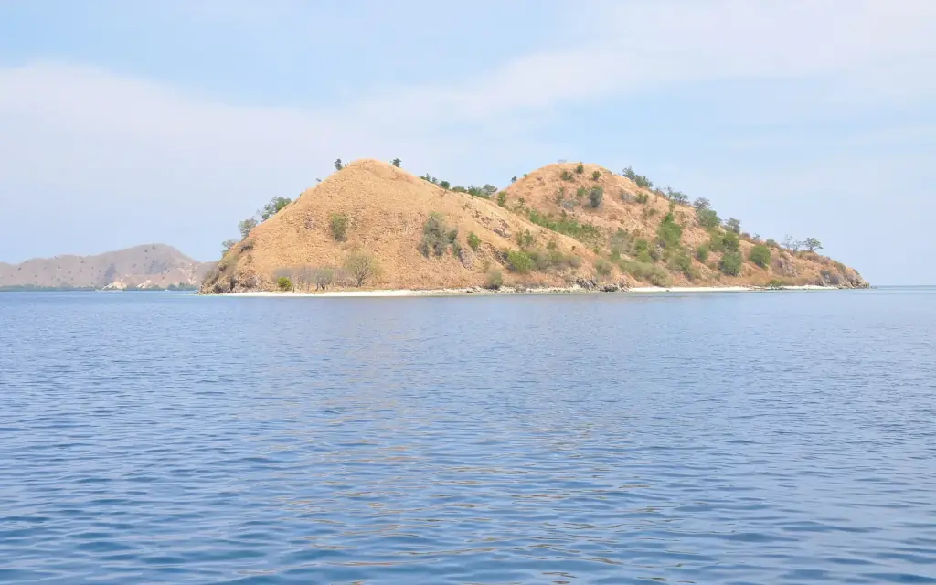 A bare, rounded island rising from flat calm sea on the boat route out of Labuan Bajo.