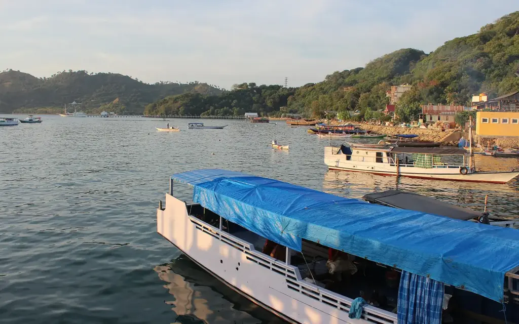 A canopied passenger boat tied up at the Labuan Bajo waterfront, with the town behind it.