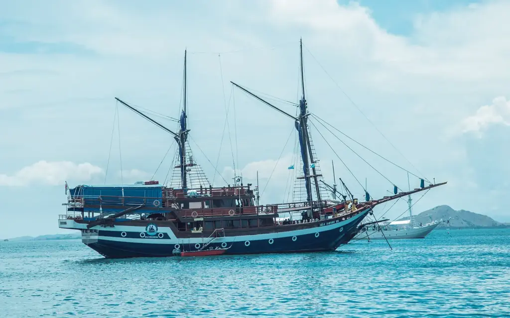 A two-masted phinisi liveaboard lying at anchor in turquoise water off Labuan Bajo.