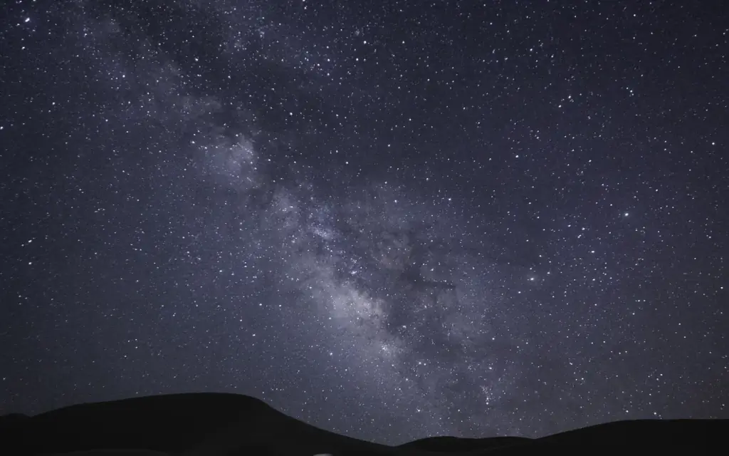 The Milky Way arching over a coastal campsite at night.