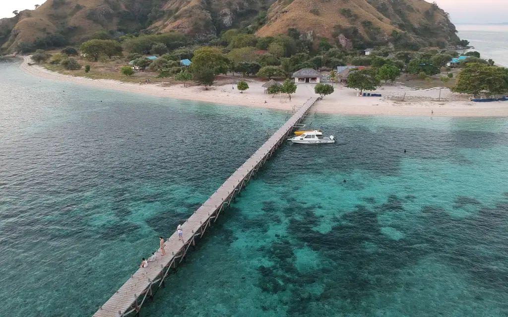 Kanawa Island from the air, photographed before resort management dismantled the wooden jetty in August 2024; the beach and green hill behind.
