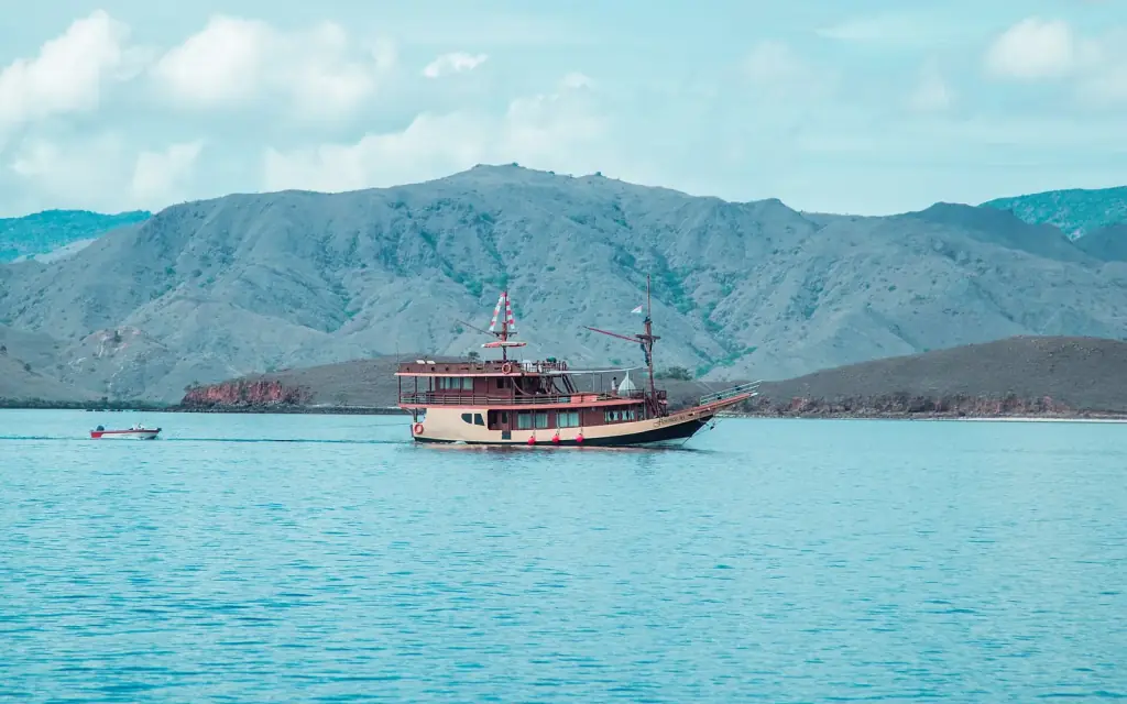 A wooden phinisi anchored in turquoise water below dry hills near Labuan Bajo.