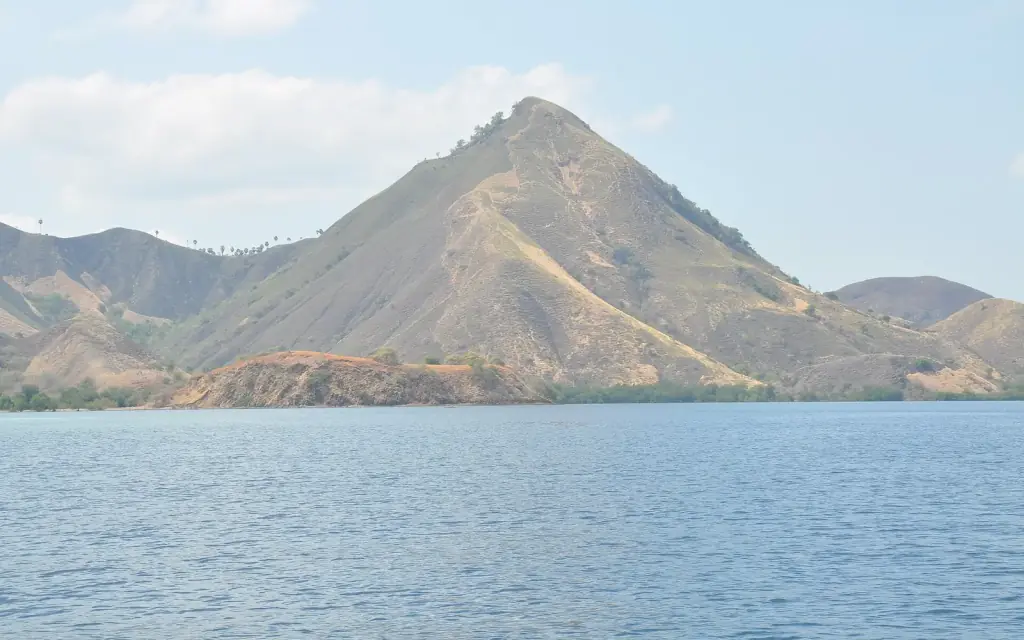A steep conical island rising from calm sea on the boat route out of Labuan Bajo.