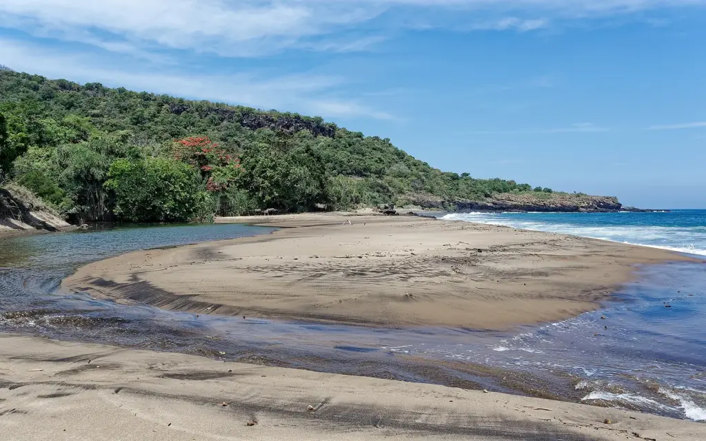 A curving beach and sandbar on the south coast of Flores, with green headlands behind.